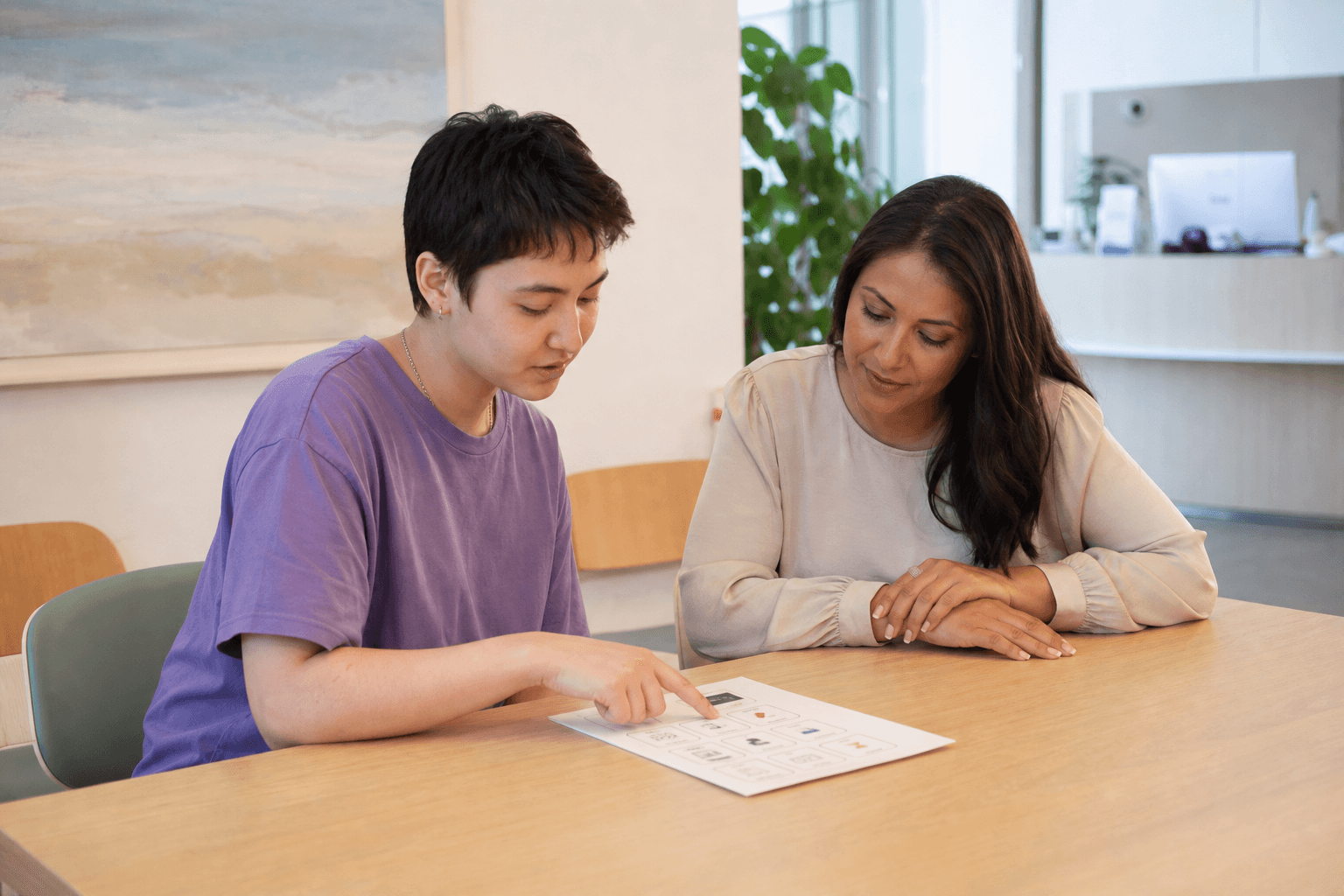 A young autistic adult chooses items on an appointment plan while a supportive adult listens beside them