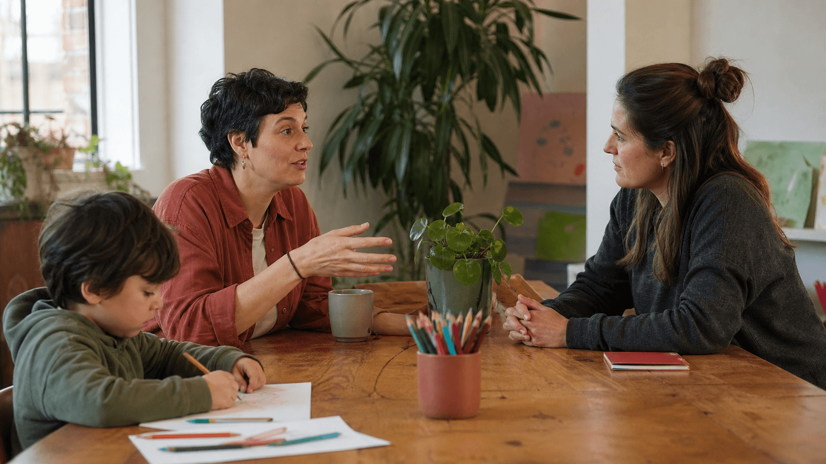 A parent and child sit with a support worker at a calm community table